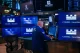 Trader in a blue jacket works at a multi-monitor trading station with Citadel Securities logos on blue screens surrounding him.
