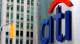 Close-up of the blue Citi logo with a red arc on a metal sign, with a blurred city street in the background.