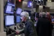 Older man with white hair shouting at multiple computer monitors on a busy trading floor.