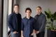 Three men stand together in a modern office near a window, posing for a group photo in casual business attire.