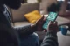 Person seated on a couch, holding a smartphone displaying a sports betting app.