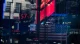 Reflection of stock quotes and corporate logos on glass storefront, including Apple, Starbucks, Nasdaq, and PayPal; red downward arrows and market numbers visible on panels.