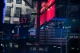 Reflection of stock quotes and corporate logos on glass storefront, including Apple, Starbucks, Nasdaq, and PayPal; red downward arrows and market numbers visible on panels.