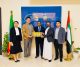Five professionals in business attire stand in a bright lobby, presenting a row of yellow boxes against a blue wall with Ethiopian and UAE flags behind them.