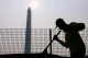 Construction worker in a high-visibility jacket leaning on a fence with the Washington Monument in the background under a hazy sun (silhouette).