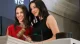 Two smiling women posing at a NYSE stage with a wooden gavel on the lectern behind glass.