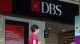 DBS bank storefront with a red logo and large DBS sign; a woman in a pink top walks by.