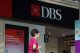 DBS bank storefront with a red logo and large DBS sign; a woman in a pink top walks by.