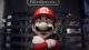 Life-size Mario statue with crossed arms, red hat, and mustache in front of a Nintendo sign at a convention.
